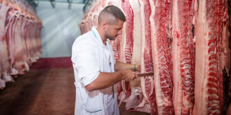 Operario trabajando en sala de procesado cárnico con pavimento industrial higiénico